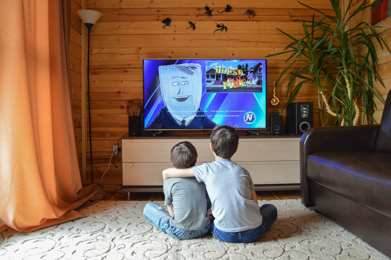 irmãos abraçados, ambos sentados no chão, olhando um desenho na Televisão